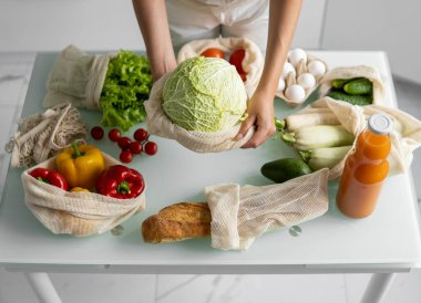 Kadın eli, evde sebzeli tekrar kullanılabilir bir market poşeti tutuyor ve lahanayı dışarı çıkarıyor. Sıfır atık ve plastiksiz konsept. Sebzeli pamuk satıcısı. Ekoloji.