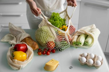 Kadın marketten döndü ve evdeki bir mutfakta sebze dolu bir poşeti açtı. Sıfır atık ve plastiksiz konsept. Kız elinde sebzeli pamuk alıcısı tutuyor..