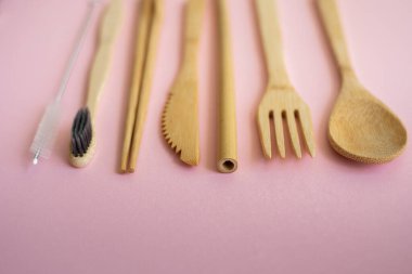 Pembe arka planda bir çantada, çevre dostu bambu çatal bıçak seti. Sıfır atık. Masanın üzerinde duran bir çantanın içindeki bambu çatal bıçak seti. Kaşık, çatal, bıçak, diş fırçası, tüp ve Çin çubukları..