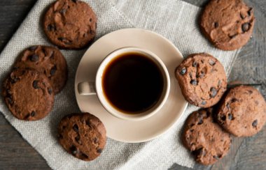 Ahşap masa arkasında kurabiyeler olan kahve fincanı. Bir fincan sade kahve ve çikolatalı kurabiye. Taze kahve çekirdekleri.
