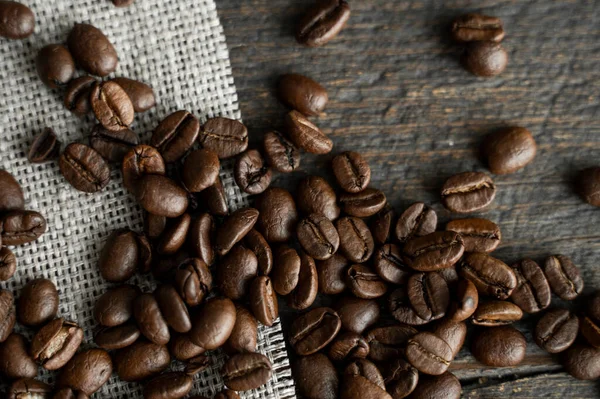 Keten tekstil üzerinde kahve çekirdekleri ve ahşap masa arkasında. Taze Arabika kahve çekirdekleri.