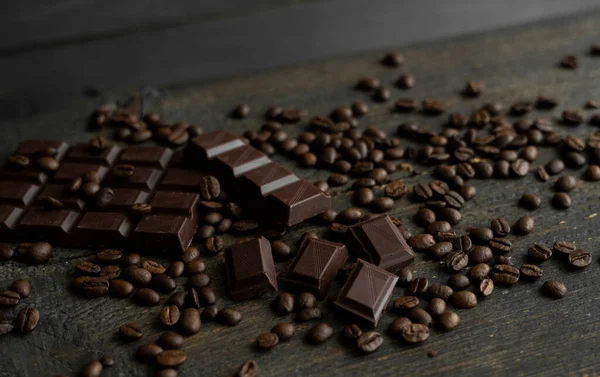 아라 비카 커피 원두는 어두운 초콜릿바가 있는 나무 탁자 위에 흩어져 있다. 신선 한 커피 콩. — 스톡 사진