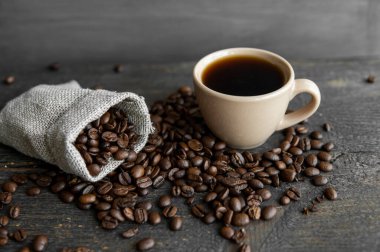 Kahve, keten bir torba ve bir fincan sade kahve Espresso ya da ahşap bir masada duran Americano 'ya saçılmış. Keten tekstil üzerine taze Arap kahvesi. Aromatik taze demlenmiş kahve..