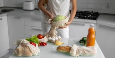 Kadın eli, evde sebzeli tekrar kullanılabilir bir market poşeti tutuyor ve lahanayı dışarı çıkarıyor. Sıfır atık ve plastiksiz konsept. Sebzeli pamuk satıcısı. Ekoloji.