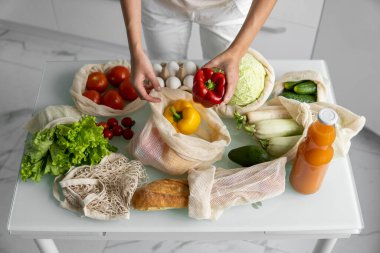 Kadın eli, evde sebzeli ve tekrar kullanılabilir bir market poşeti tutuyor ve biberi çıkarıyor. Sıfır atık ve plastiksiz konsept. Sebzeli pamuk satıcısı. Ekoloji.
