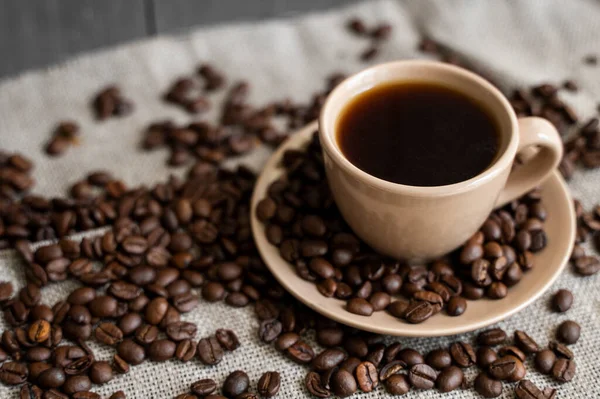 Кофейная чашка с жареными кофейными зернами на льняном фоне. Кружка черного кофе с разбросанными кофейными зёрнами. Свежий кофе в зернах. — стоковое фото