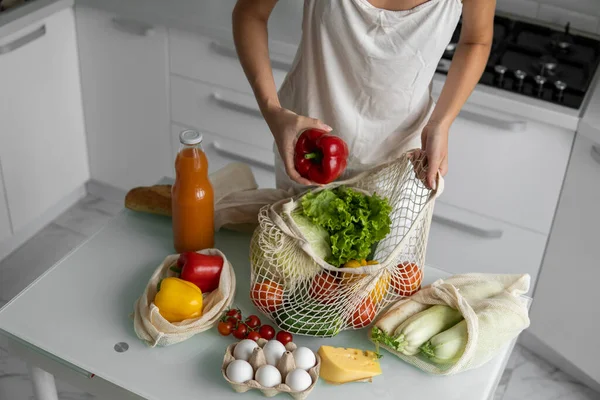 Mujeres de la mano, sosteniendo una bolsa de comestibles reutilizable con verduras en una cocina en casa y saca pimienta. Cero residuos y concepto libre de plástico. Comprador de algodón de malla con verduras. Ecología. — Foto de Stock