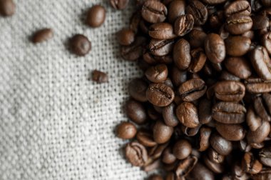 Keten tekstil üzerinde kahve çekirdekleri ve ahşap masa arkasında. Taze Arabika kahve çekirdekleri.