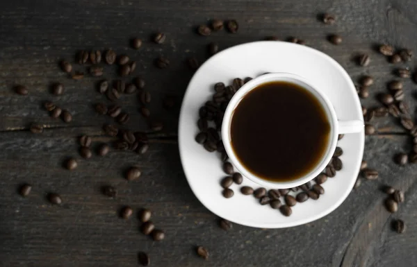 stock image Coffee cup with roasted coffee beans on wooden table background. Mug of black coffe with scattered coffee beans on a wooden table. Fresh coffee beans.