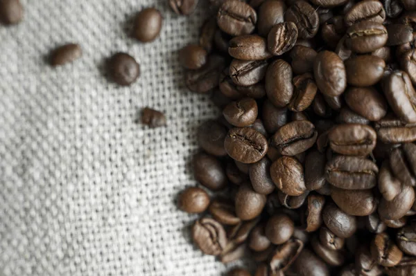 Grãos de café em um tecido de linho e em um fundo de mesa de madeira. Grãos de café arábica frescos. — Fotografia de Stock