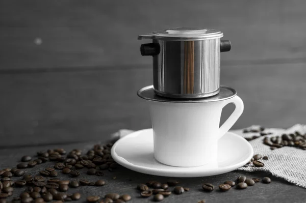 Xícara branca de café com um filtro metálico em um topo e feijões espalhados em uma mesa de madeira. Café vietnamita tradicional. — Fotografia de Stock