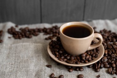 Keten arka planda kavrulmuş kahve çekirdekli kahve fincanı. Bir kupa sade kahve ve dağınık kahve çekirdeği. Taze kahve çekirdekleri.