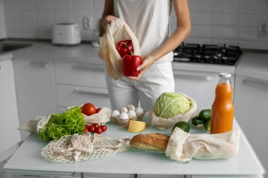 Kadın eli, evde sebzeli ve tekrar kullanılabilir bir market poşeti tutuyor ve biberi çıkarıyor. Sıfır atık ve plastiksiz konsept. Sebzeli pamuk satıcısı. Ekoloji.