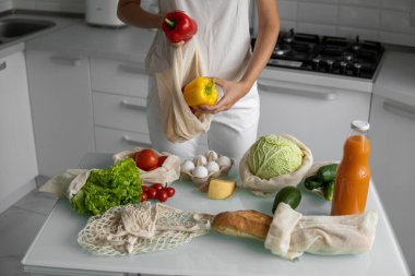 Kadın eli, evde sebzeli ve tekrar kullanılabilir bir market poşeti tutuyor ve biberi çıkarıyor. Sıfır atık ve plastiksiz konsept. Sebzeli pamuk satıcısı. Ekoloji.