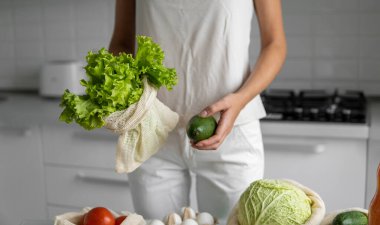 Kadın eli, evde sebzeli tekrar kullanılabilir bir poşet tutuyor ve salata ile avokadoyu dışarı çıkarıyor. Sıfır atık ve plastiksiz konsept. Sebzeli pamuk satıcısı. Ekoloji.