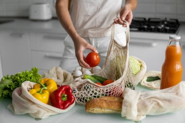 Kadın eli, evde sebzeli bir poşet tutuyor ve domatesi dışarı çıkarıyor. Sıfır atık ve plastiksiz konsept. Sebzeli pamuk satıcısı. Ekoloji.