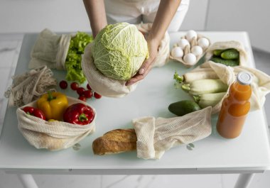 Kadın eli, evde sebzeli tekrar kullanılabilir bir market poşeti tutuyor ve lahanayı dışarı çıkarıyor. Sıfır atık ve plastiksiz konsept. Sebzeli pamuk satıcısı. Ekoloji.
