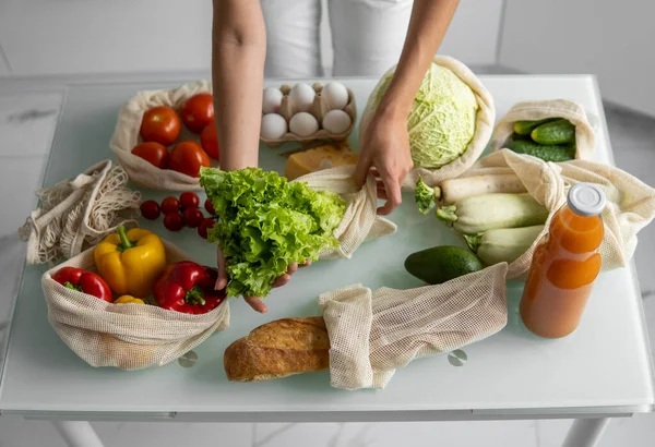 Womans hand, holding a reusable grocery bag with vegetables on a kitchen at home and takes salad out. Zero waste and plastic free concept. Mesh cotton shopper with vegetables. Ecology. — Stock Photo, Image