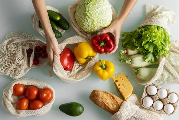 Womans hand, holding a reusable grocery bag with vegetables on a kitchen at home and takes pepper out. Zero waste and plastic free concept. Mesh cotton shopper with vegetables. Ecology. — Stock Photo, Image