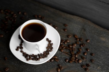 Ahşap masa arkasında kavrulmuş kahve çekirdekli kahve fincanı. Bir kupa sade kahve ve ahşap bir masanın üzerinde kahve çekirdekleri. Taze kahve çekirdekleri.