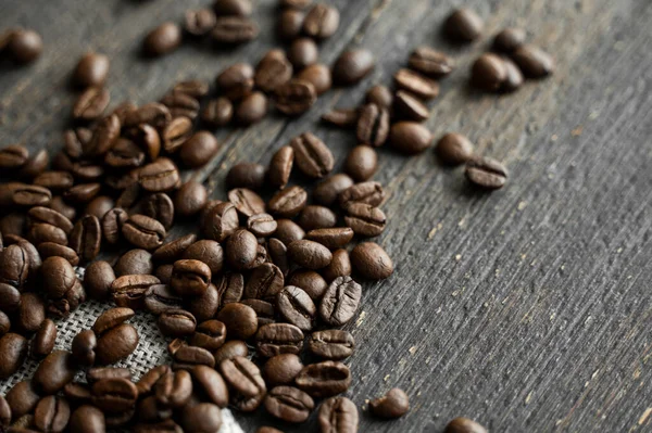 Grãos de café em um tecido de linho e em um fundo de mesa de madeira. Grãos de café arábica frescos. — Fotografia de Stock