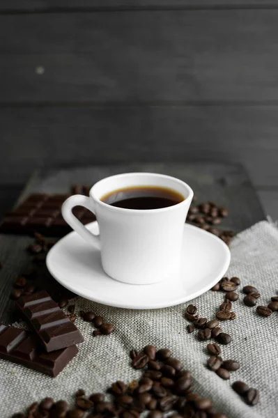 코 오피 컵 에 쿠키 와 초컬릿 을 넣고 커피 원두를 아마포와 나무 식탁 위에 펼쳐 놓는다. 검은 커피 덩어리. — 스톡 사진