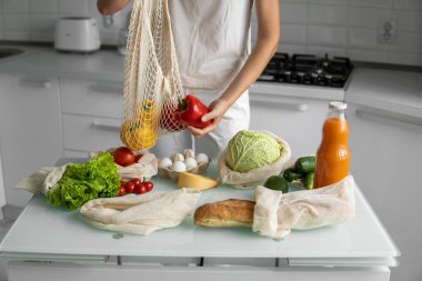 Kadın eli, evde sebzeli ve tekrar kullanılabilir bir market poşeti tutuyor ve biberi çıkarıyor. Sıfır atık ve plastiksiz konsept. Sebzeli pamuk satıcısı. Ekoloji.