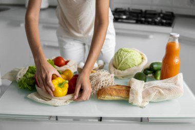 Kadın eli, evde sebzeli ve tekrar kullanılabilir bir market poşeti tutuyor ve biberi çıkarıyor. Sıfır atık ve plastiksiz konsept. Sebzeli pamuk satıcısı. Ekoloji.
