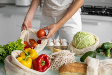 Kadın eli, evde sebzeli bir poşet tutuyor ve domatesi dışarı çıkarıyor. Sıfır atık ve plastiksiz konsept. Sebzeli pamuk satıcısı. Ekoloji.
