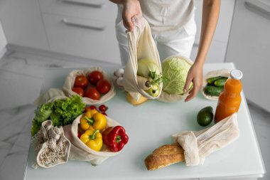 Kadın marketten döndü ve evdeki bir mutfakta sebze dolu bir poşeti açtı. Sıfır atık ve plastiksiz konsept. Kız elinde sebzeli pamuk alıcısı tutuyor..
