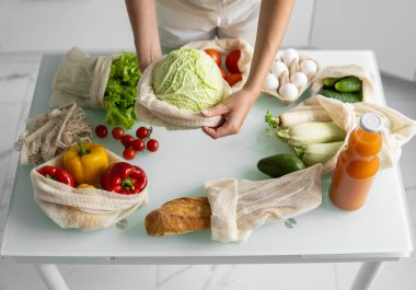 Kadın eli, evde sebzeli tekrar kullanılabilir bir market poşeti tutuyor ve lahanayı dışarı çıkarıyor. Sıfır atık ve plastiksiz konsept. Sebzeli pamuk satıcısı. Ekoloji.