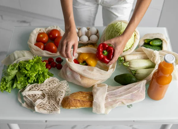 Womans hand, holding a reusable grocery bag with vegetables on a kitchen at home and takes pepper out. Zero waste and plastic free concept. Mesh cotton shopper with vegetables. Ecology. — Stock Photo, Image