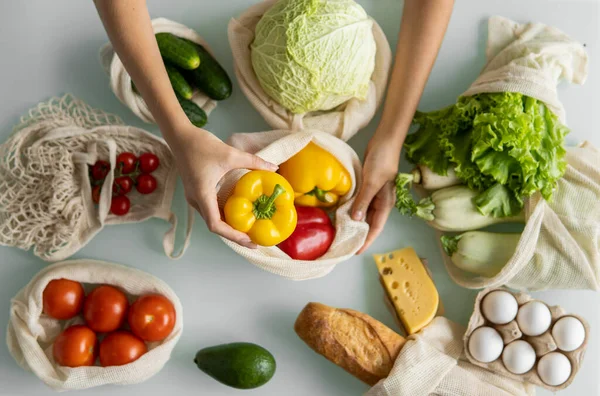 Vrouwen hand, houden een herbruikbare kruidenierszak met groenten op een keuken thuis en neemt peper uit. Geen afval en plastic vrij concept. Mesh katoenen shopper met groenten. Ecologie. — Stockfoto