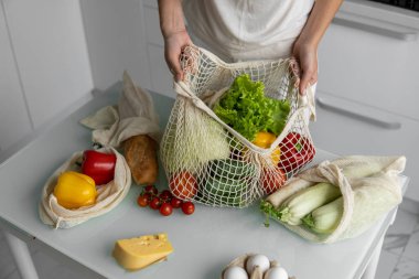 Kadın marketten döndü ve evdeki bir mutfakta sebze dolu bir poşeti açtı. Sıfır atık ve plastiksiz konsept. Kız elinde sebzeli pamuk alıcısı tutuyor..