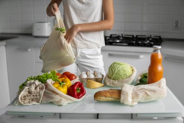 Yeniden kullanılabilir ekolojik bakkal poşeti ve sebze ve meyve tutan kadın. Sıfır atık ve plastiksiz konsept. Kız elinde sebzeli pamuk alıcısı tutuyor..