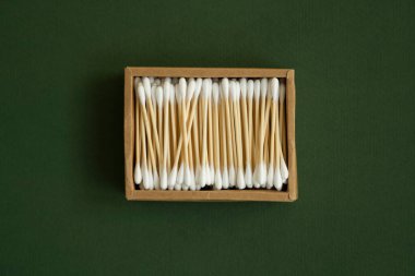 Çevre dostu pamuklu çubuklar. Yeşil bir yüzey üzerinde geri dönüşümlü bambu tomurcukları içeren karton bir kutu. Sıfır atık. Eko ürün. Kozmetik çubuklar kutuda. Kulakları temizlemek için tahta sopalar..
