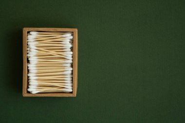 Çevre dostu pamuklu çubuklar. Yeşil bir yüzey üzerinde geri dönüşümlü bambu tomurcukları içeren karton bir kutu. Sıfır atık. Eko ürün. Kozmetik çubuklar kutuda. Kulakları temizlemek için tahta sopalar..
