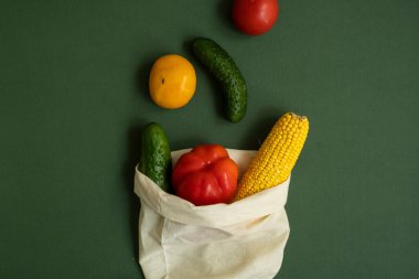 Yeşil yüzeyde sebzeler eko torbanın içinde. Biber, domates, mısır, salatalık, brokoli, tekrar kullanılabilir alışveriş ekosu dostu pamuk torbalarda karnabahar. Sıfır atık ve plastiksiz konsept. Sürdürülebilir.