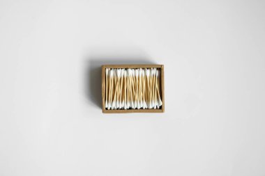 Çevre dostu pamuklu çubuklar. Gri bir yüzey üzerinde geri dönüşümlü bambu tomurcukları içeren karton bir kutu. Sıfır atık. Eko ürün. Kozmetik çubuklar kutuda. Kulakları temizlemek için tahta sopalar..