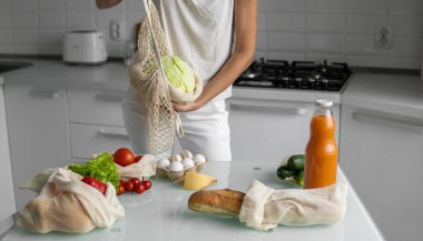 Kadın eli, evde sebzeli tekrar kullanılabilir bir market poşeti tutuyor ve lahanayı dışarı çıkarıyor. Sıfır atık ve plastiksiz konsept. Sebzeli pamuk satıcısı. Ekoloji.