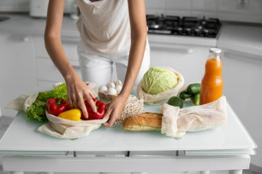 Kadın eli, evde sebzeli ve tekrar kullanılabilir bir market poşeti tutuyor ve biberi çıkarıyor. Sıfır atık ve plastiksiz konsept. Sebzeli pamuk satıcısı. Ekoloji.