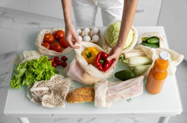 Kadın eli, evde sebzeli ve tekrar kullanılabilir bir market poşeti tutuyor ve biberi çıkarıyor. Sıfır atık ve plastiksiz konsept. Sebzeli pamuk satıcısı. Ekoloji.