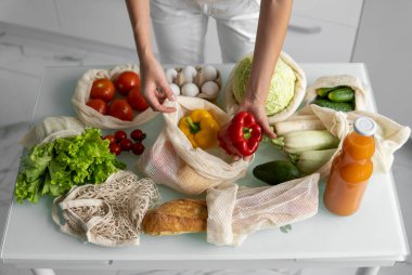 Kadın eli, evde sebzeli ve tekrar kullanılabilir bir market poşeti tutuyor ve biberi çıkarıyor. Sıfır atık ve plastiksiz konsept. Sebzeli pamuk satıcısı. Ekoloji.