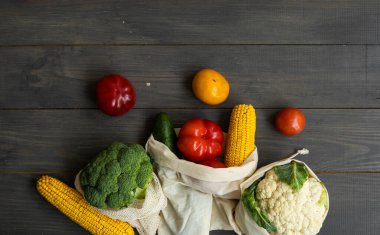 Sıfır atık. Biber, domates, mısır, salatalık, brokoli, tekrar kullanılabilir alışveriş ekosu dostu pamuk torbalarda karnabahar. Tahta bir masada sebzeler eko torbanın içinde. Plastiksiz konsept.