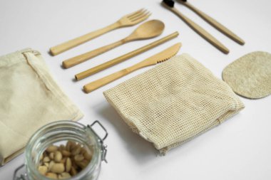 Sıfır atık. Çevre dostu bambu çatal bıçak takımı, ağ pamuk torbaları, bambu diş fırçası, cam kavanozlar ve lif süngeri. Plastiksiz. Gri yüzeyde doğal ve yeniden kullanılabilir öğeler aksesuarları.