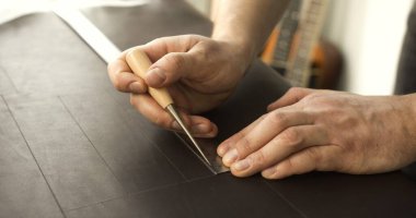 Close up of leather craftsman hands measuring and drawing straight lines on leather using awl and ruler for precise cutting.