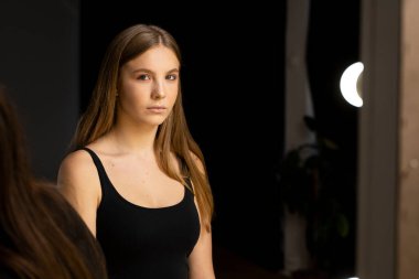 Young woman with long straight hair and natural makeup posing in dark studio background.