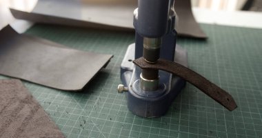 Leather strip pressed with machine in workshop. Step in traditional handmade leather crafting for punching holes and shaping accessories.