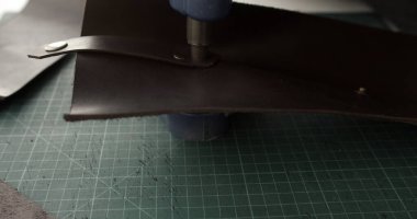 Perçinle sabitlenmiş deri kayış. Yeşil kesme paspasının üzerinde pres makinesi var. Aksesuar üretimi için geleneksel el yapımı deri işçiliğine geçin.