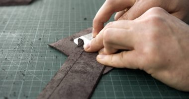 Craftsman hands skiving leather strip to achieve thinner surface. Step in handmade leather accessory making, performed with precision.